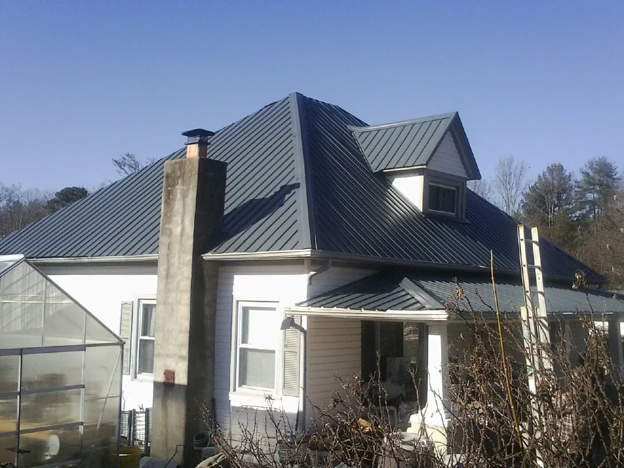 Dark blue standing seam metal roof on a white farmhouse with dormer — Slate & Tile Roof Repair by Roofing Brothers in Port Jefferson