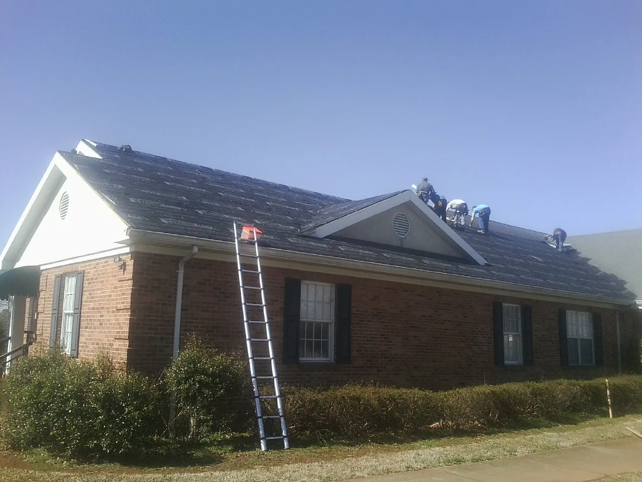 Crew tearing shingles off a brick ranch roof with a ladder set — Emergency Roof Repair work by our crew in Port Jefferson