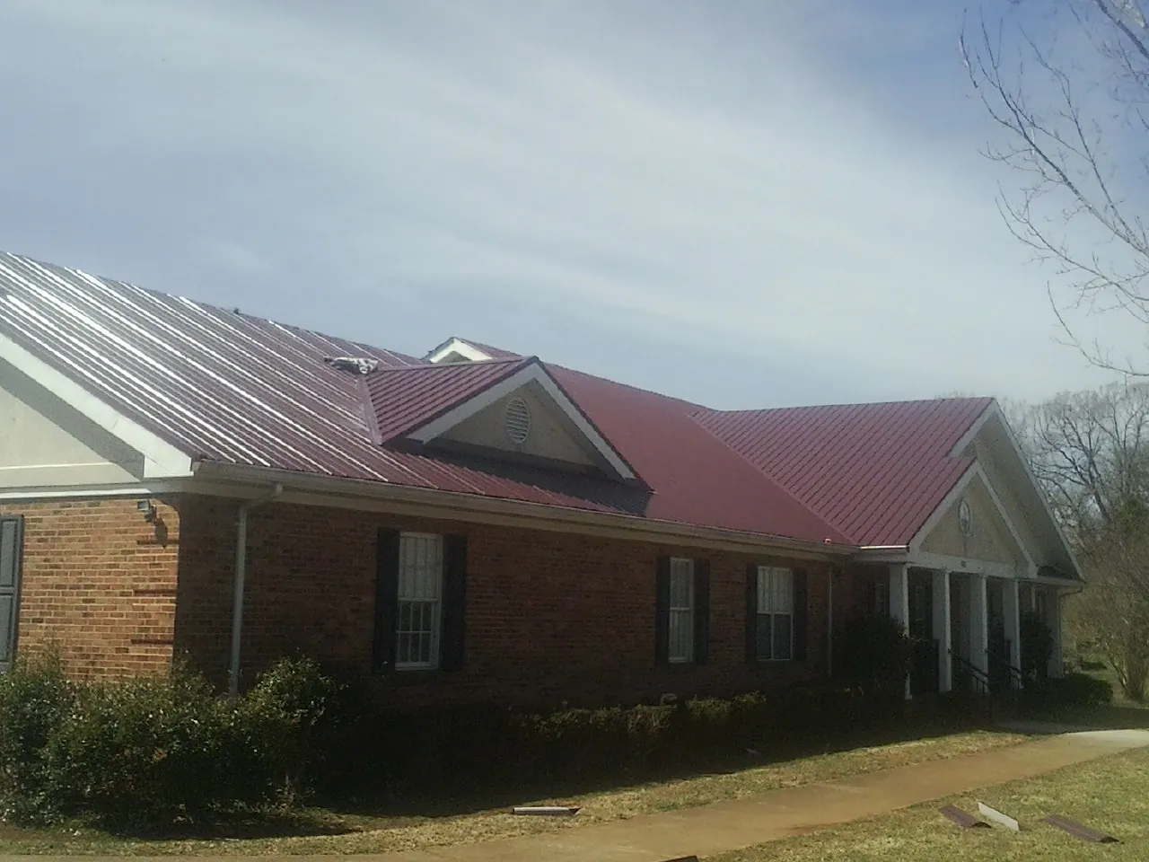 Red metal roof with gabled entries on a long brick building, from a Hail Damage Roof Repair job in Port Jefferson