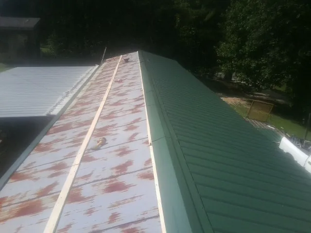 Old rusted panels beside newly installed green metal roofing — Wind Damage Roof Repair by Roofing Brothers in Port Jefferson