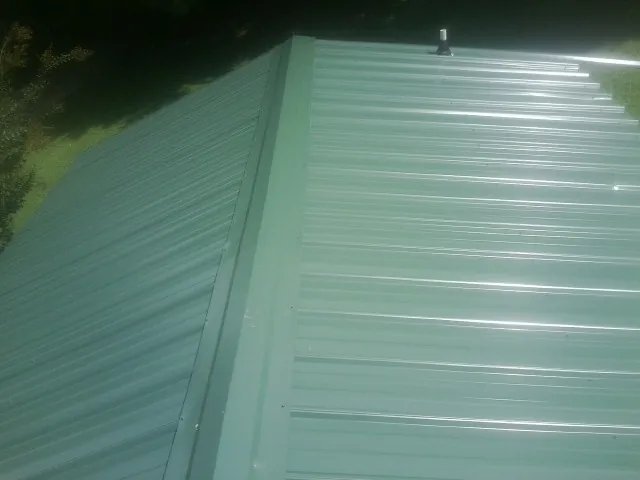 New green metal panels meeting at the ridge of a roof — Flat Roof Repair work by our crew in Port Jefferson