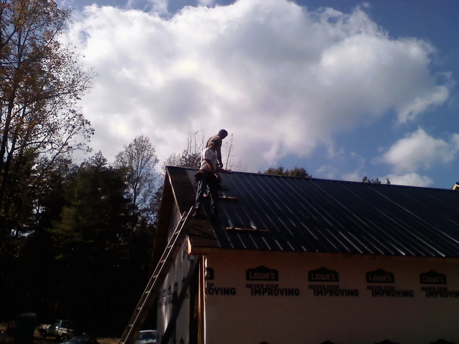 Roofer fastening dark metal panels high against a cloudy sky, from a Roof Inspection job in Port Jefferson