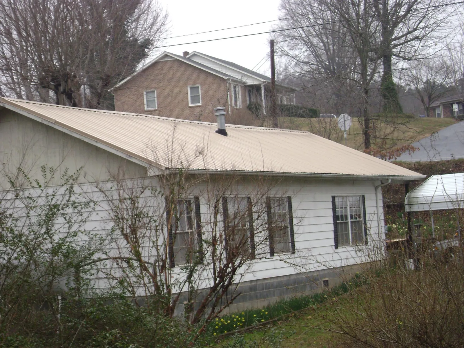 Tan metal roof on a white sided house set into a hillside — Commercial Roofing by Roofing Brothers in Port Jefferson