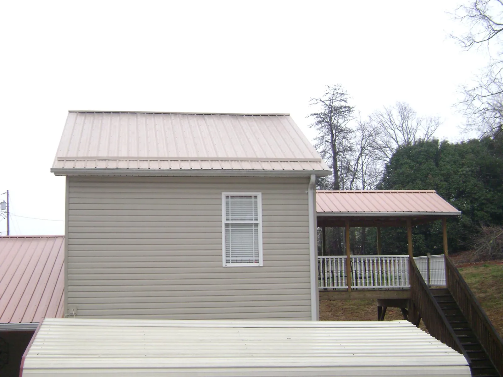 Tan metal roofs on a two story addition and attached porch, from a Roof Replacement job in Port Jefferson